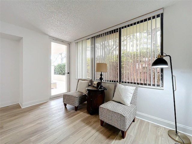 living area featuring floor to ceiling windows, a textured ceiling, baseboards, and wood finished floors