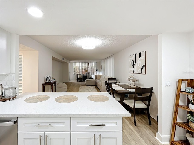 kitchen featuring white cabinets, light wood-style flooring, light stone countertops, a textured ceiling, and backsplash