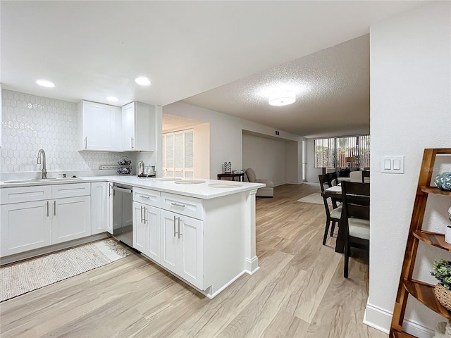 kitchen featuring white cabinets, a peninsula, a sink, light countertops, and stainless steel dishwasher