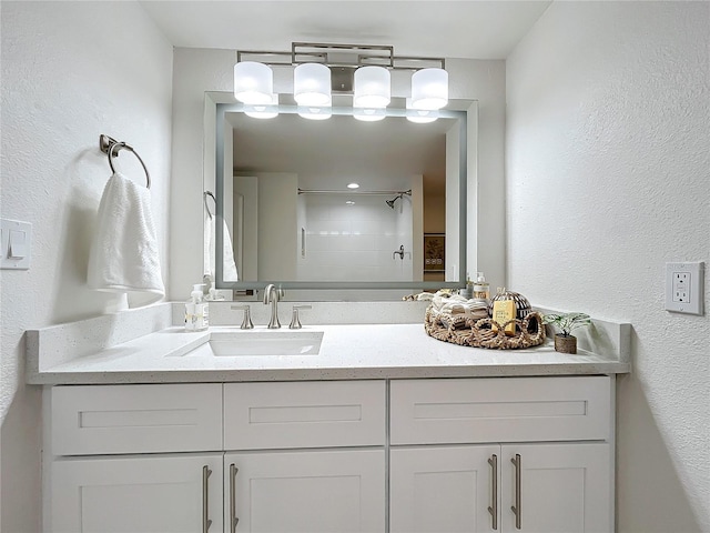 bathroom with tiled shower, a textured wall, and vanity