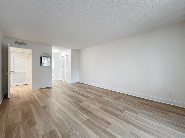 empty room with baseboards, a textured ceiling, visible vents, and wood finished floors