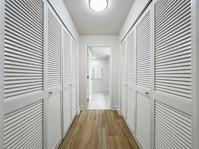 hall with baseboards, a textured ceiling, and wood finished floors