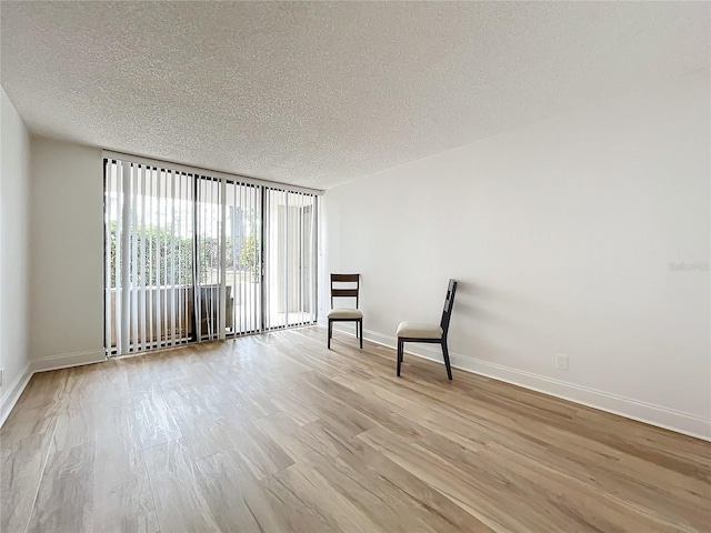 unfurnished room with light wood-type flooring, baseboards, and a textured ceiling