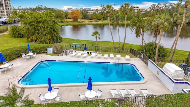 pool with a patio, grilling area, a water view, fence, and a yard