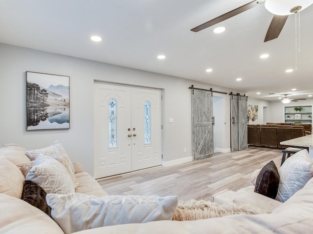 living room featuring ceiling fan, a barn door, and light hardwood / wood-style flooring