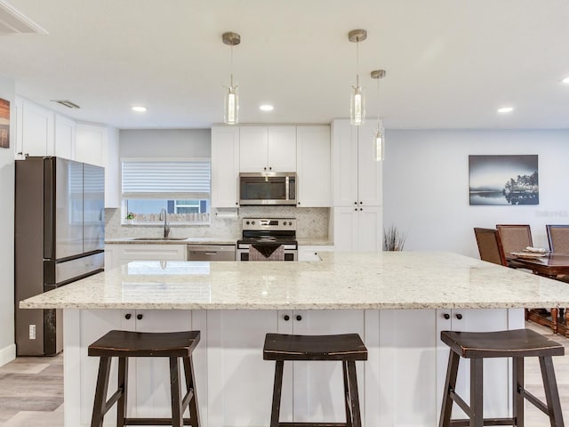 kitchen with a spacious island, sink, white cabinetry, decorative light fixtures, and stainless steel appliances