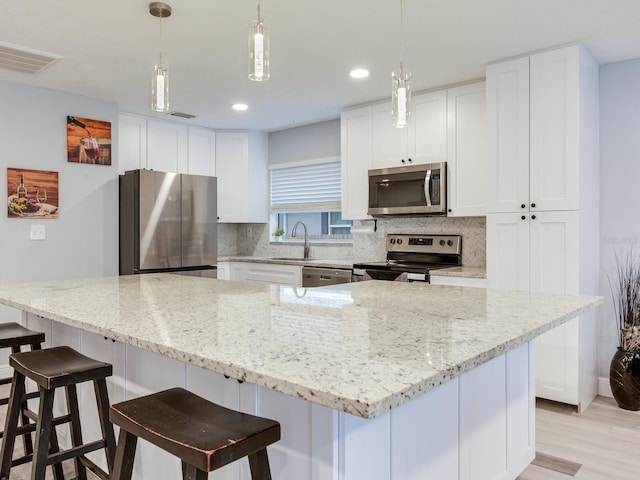 kitchen featuring a spacious island, white cabinetry, light stone counters, pendant lighting, and stainless steel appliances