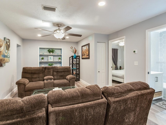 living room with a textured ceiling, ceiling fan, and light wood-type flooring