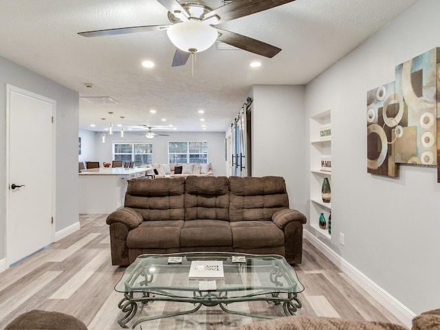 living room featuring built in shelves, a textured ceiling, and light hardwood / wood-style flooring