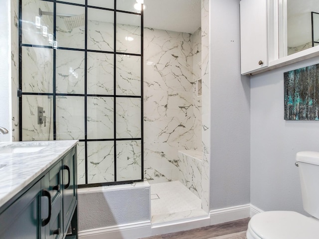 bathroom featuring hardwood / wood-style flooring, vanity, toilet, and a tile shower