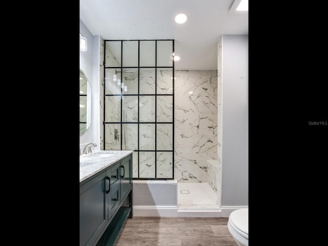 bathroom with a tile shower, vanity, hardwood / wood-style flooring, and toilet