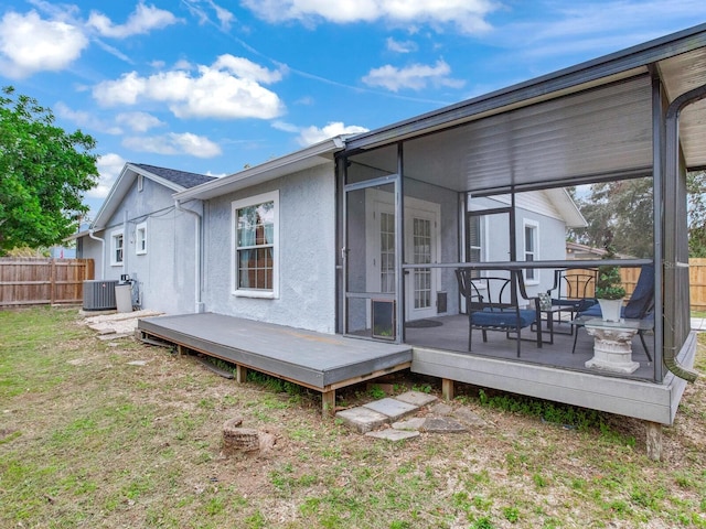 back of property featuring a wooden deck, a lawn, a sunroom, and central air condition unit