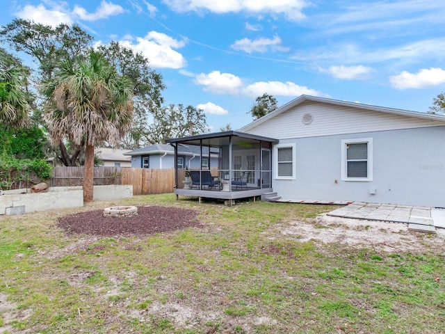 back of property with a lawn, a sunroom, and an outdoor fire pit