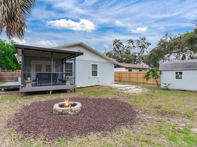 rear view of property featuring a storage shed, a fire pit, a lawn, a wooden deck, and a sunroom