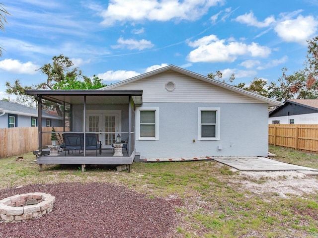 rear view of property featuring a deck, a fire pit, a yard, a sunroom, and french doors