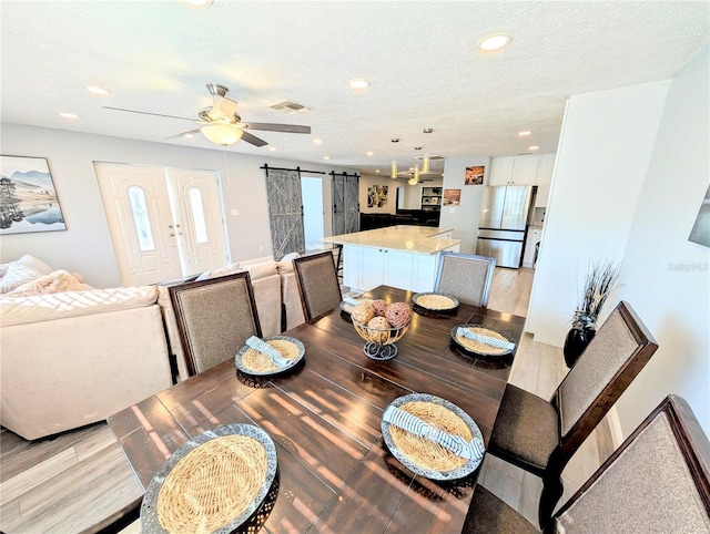 dining space with ceiling fan, light hardwood / wood-style floors, a barn door, a healthy amount of sunlight, and a textured ceiling