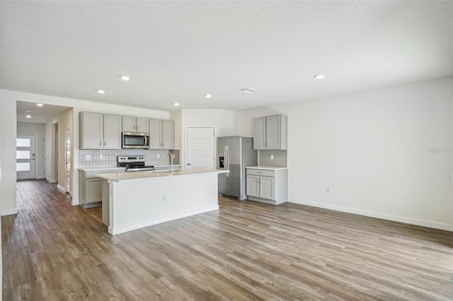 kitchen featuring gray cabinets, backsplash, a center island with sink, and stainless steel appliances