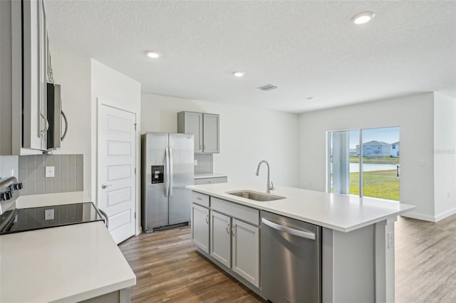 kitchen with a textured ceiling, appliances with stainless steel finishes, sink, backsplash, and a center island with sink