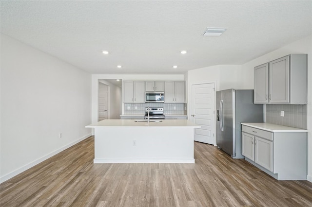 kitchen with a center island with sink, appliances with stainless steel finishes, decorative backsplash, and gray cabinets