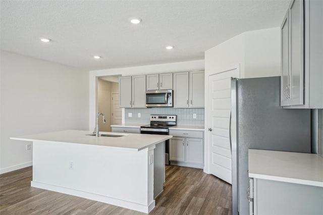 kitchen featuring dark hardwood / wood-style flooring, stainless steel appliances, decorative backsplash, sink, and a center island with sink