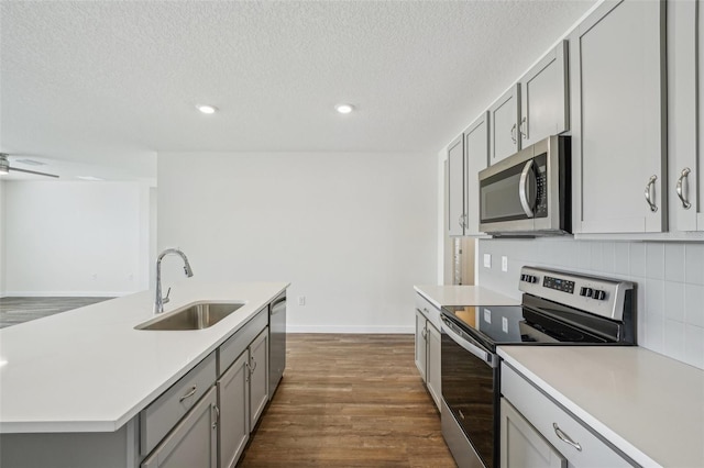 kitchen featuring appliances with stainless steel finishes, a textured ceiling, gray cabinetry, sink, and a center island with sink