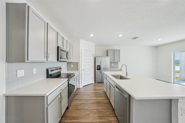 kitchen featuring appliances with stainless steel finishes, a textured ceiling, a kitchen island with sink, sink, and gray cabinets