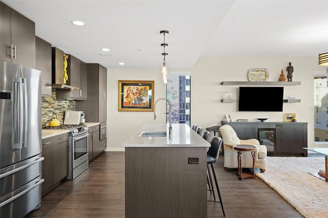 kitchen with an island with sink, appliances with stainless steel finishes, backsplash, dark wood-type flooring, and sink