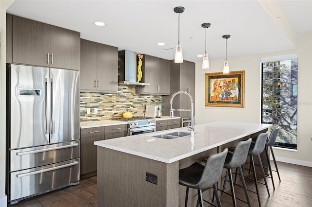 kitchen featuring stainless steel appliances, decorative backsplash, wall chimney exhaust hood, light stone counters, and sink