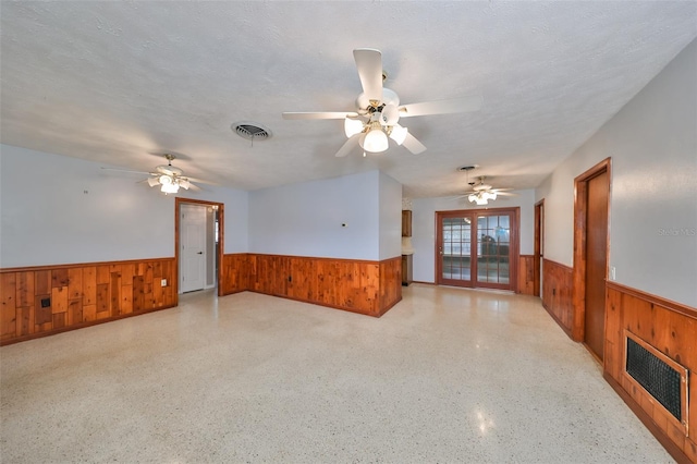 unfurnished room with a textured ceiling, ceiling fan, and wood walls