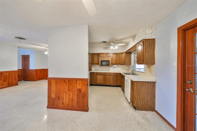 kitchen with white dishwasher, sink, ceiling fan, and wooden walls