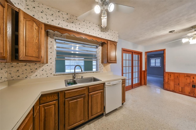 kitchen featuring french doors, wooden walls, ceiling fan, sink, and white dishwasher