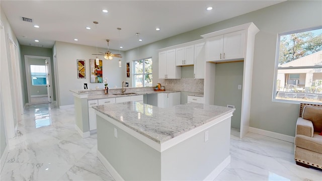 kitchen featuring ceiling fan, a center island, decorative light fixtures, white cabinets, and sink