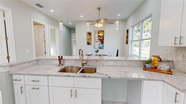 kitchen with pendant lighting, decorative backsplash, sink, white cabinets, and light stone counters