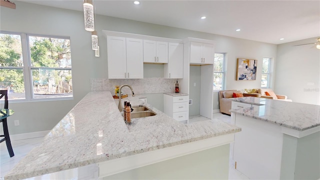 kitchen featuring white cabinets, sink, backsplash, hanging light fixtures, and kitchen peninsula