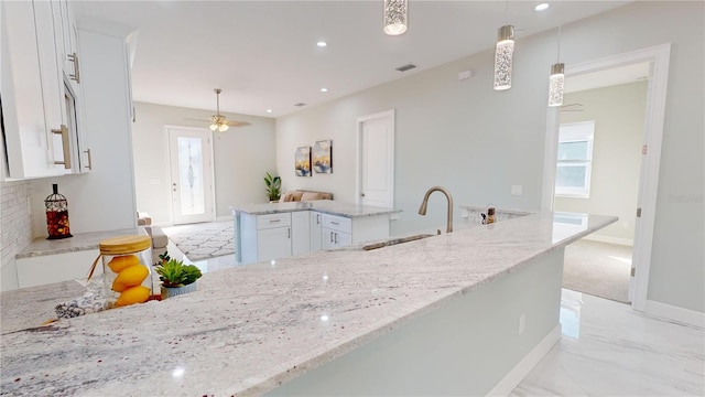 kitchen with pendant lighting, white cabinets, sink, ceiling fan, and light stone counters