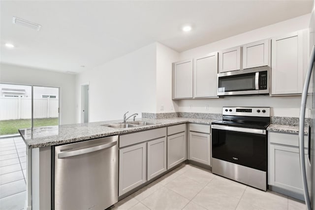 kitchen with kitchen peninsula, sink, appliances with stainless steel finishes, light tile patterned floors, and light stone counters