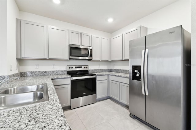 kitchen with light tile patterned floors, appliances with stainless steel finishes, gray cabinetry, light stone counters, and sink