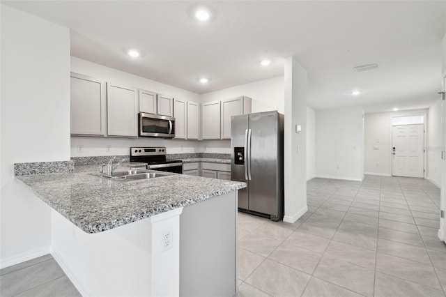 kitchen with stainless steel appliances, sink, kitchen peninsula, light stone counters, and light tile patterned floors