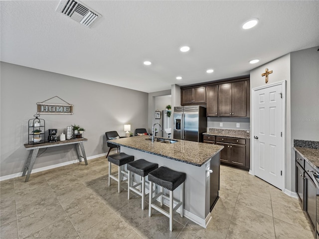 kitchen with stainless steel refrigerator with ice dispenser, sink, a kitchen island with sink, and a breakfast bar