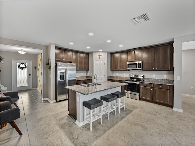 kitchen with appliances with stainless steel finishes, sink, a kitchen breakfast bar, a kitchen island with sink, and light stone counters