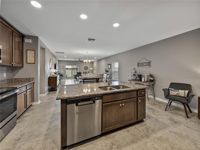 kitchen with stainless steel appliances, an island with sink, sink, stone countertops, and dark brown cabinets