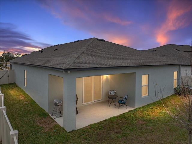 back house at dusk featuring a patio area and a yard