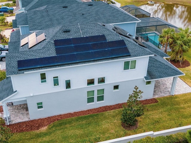 exterior space with glass enclosure, a water view, a lawn, and solar panels