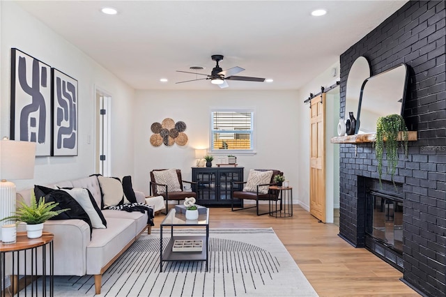 living room featuring a large fireplace, light hardwood / wood-style floors, a barn door, and ceiling fan