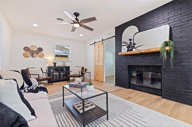 living room featuring ceiling fan, a barn door, a fireplace, and light wood-type flooring