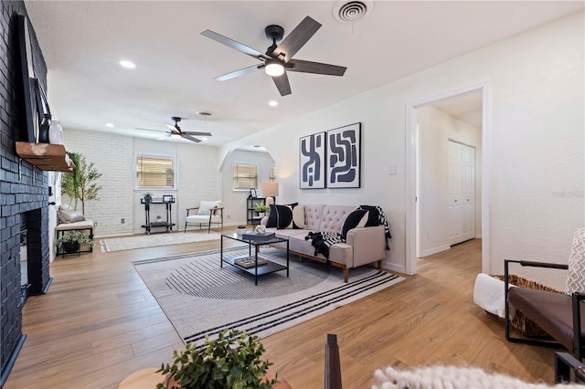 living room featuring a brick fireplace, light hardwood / wood-style floors, and ceiling fan