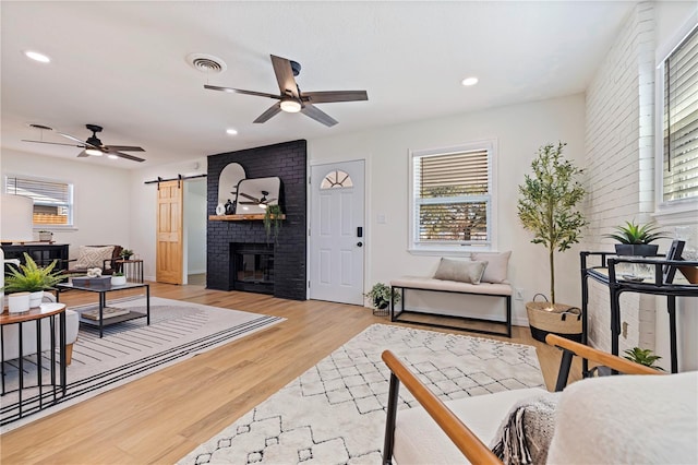 living room featuring ceiling fan, a barn door, a fireplace, and light hardwood / wood-style floors