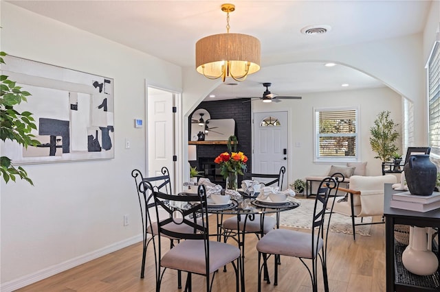 dining space with ceiling fan, a fireplace, and light hardwood / wood-style flooring