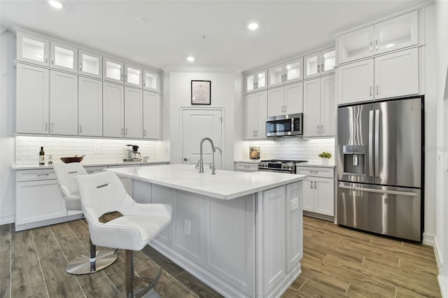 kitchen featuring backsplash, white cabinets, a kitchen breakfast bar, stainless steel appliances, and a center island with sink