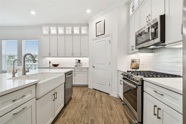 kitchen featuring stainless steel appliances, white cabinetry, sink, and crown molding